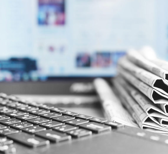 Eine Zeitung liegt neben einer Computer-Tastatur. Im Hintergrund ist ein Computer-Monitor sichtbar.